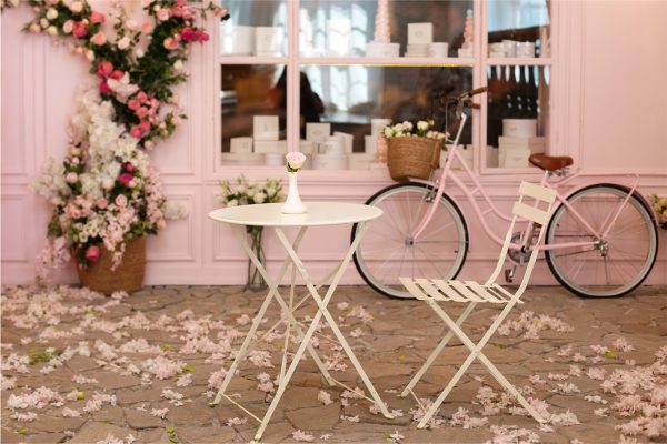 Fransk romantisk cafe i lyserøde farver, med nedfaldende kirsebærblomster og en cykel parkeret ved facaden af cafeen