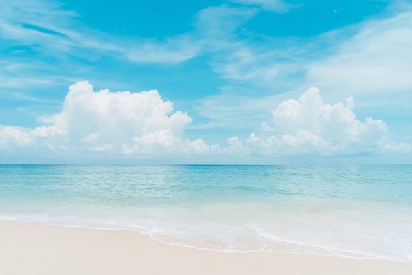 Strand i lyse og drømmende farver, det næsten hvide sand og den lyse blå himmel med lette skyder.