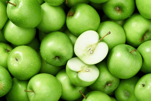 Grønne syrlige granny smith æbler fylder hele baggrunden og et enkel æble et skrået i halve