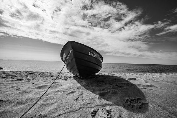 Træbåd der ligger på stranden, billedet er taget nedefra, og er i grå nuancer