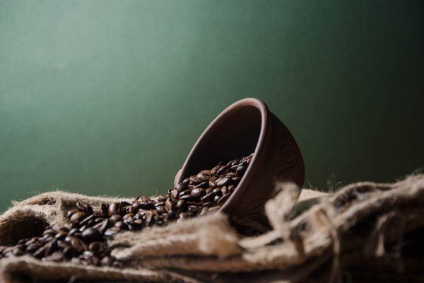 Skål der ligger i en sæk med kaffebønner, billedet har grå baggrund