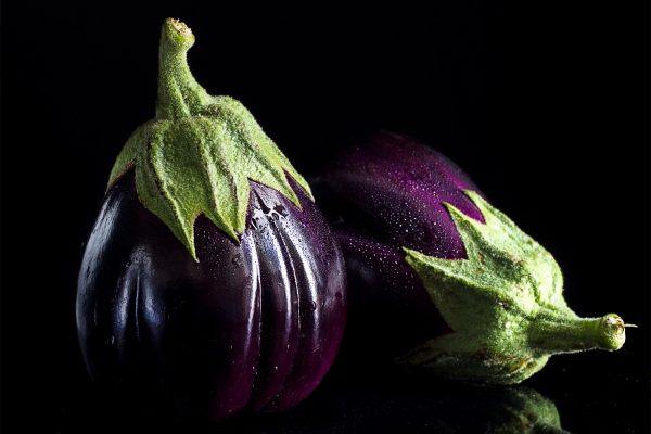 Aubergine der ligger og står med vanddråber. Billedet er tage i sorte omgivelser